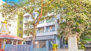 Un edificio residencial con varios balcones, entrada con portón y un árbol en primer plano.