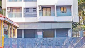 Un edificio de varios pisos con fachada blanca, ventanas amplias y entrada con persianas cerradas.