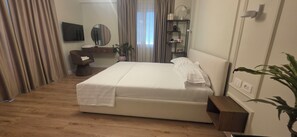 Ein Hotelzimmer mit Bett, Schreibtisch, Stuhl, Spiegel, Pflanze und einem Fenster mit Vorhängen.