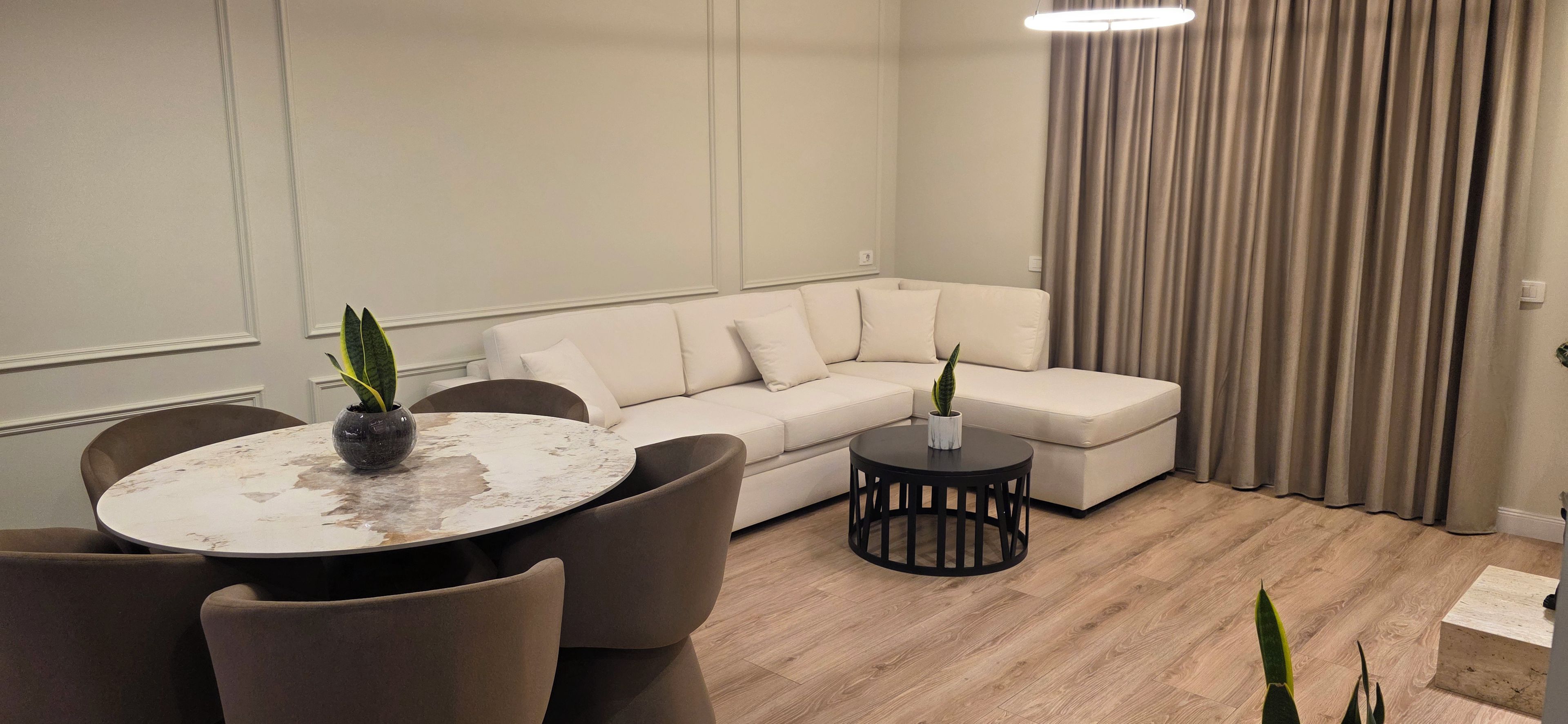 Un salon moderne avec une table à manger ronde, un canapé et deux tables d’appoint, chacune agrémentée d’une plante en pot.