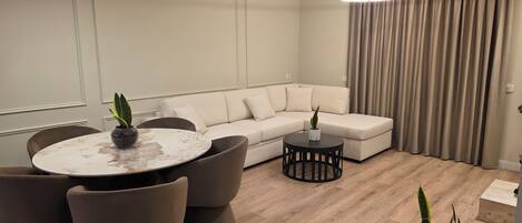 A modern living room with a round dining table, a sofa, and two side tables, each with a potted plant.