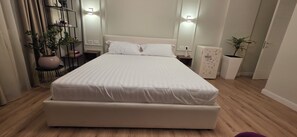 Une chambre à coucher bien rangée, avec un grand lit, des tables de chevet, une étagère remplie de livres et une plante en pot.