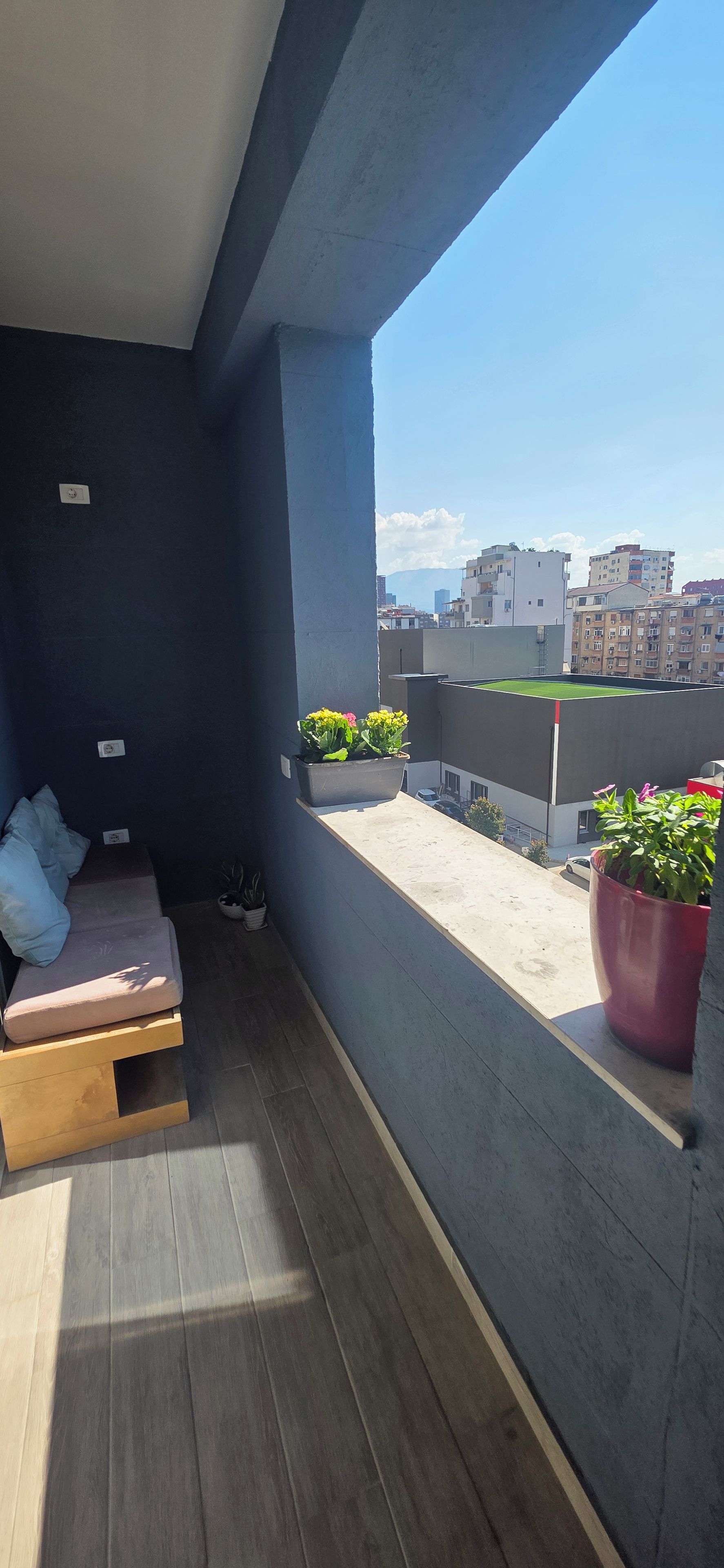 A balcony with a seating area, potted plants, and a view of the cityscape.