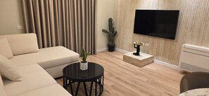 Un salon moderne avec un canapé, une table basse, un cactus, une statue et un téléviseur à écran plat fixé au mur.