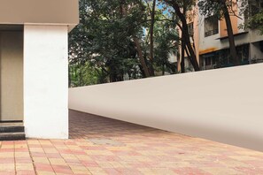 A paved outdoor area with a white wall and trees in the background. - Townhouse Oak Hadapsar Sahyadri Hospital (Pune)