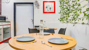 A dining area with a round table, chairs, and plates. There is a door, a clock, and a framed picture on the wall.