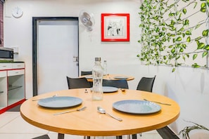 A dining area with a round table, chairs, and plates. There is a door, a clock, and a framed picture on the wall. - Townhouse Oak Hadapsar Sahyadri Hospital (Pune)