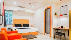 Habitación de hotel con cama, sofá naranja, escritorio y ventilador de techo.