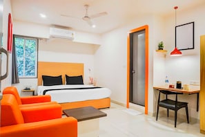 Une chambre d’hôtel avec un lit, un canapé orange, un bureau et un ventilateur de plafond.