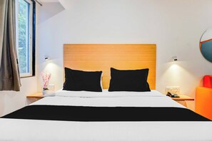 A hotel room with a wooden headboard, two black pillows, a white bedspread, a bedside table with a lamp, a telephone, and a red chair. - Townhouse Oak Hadapsar Sahyadri Hospital (Pune)