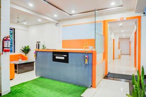 Un espace d’accueil avec un bureau bleu et orange, un extincteur et un panneau indiquant qu’il est entretenu par l’entreprise.