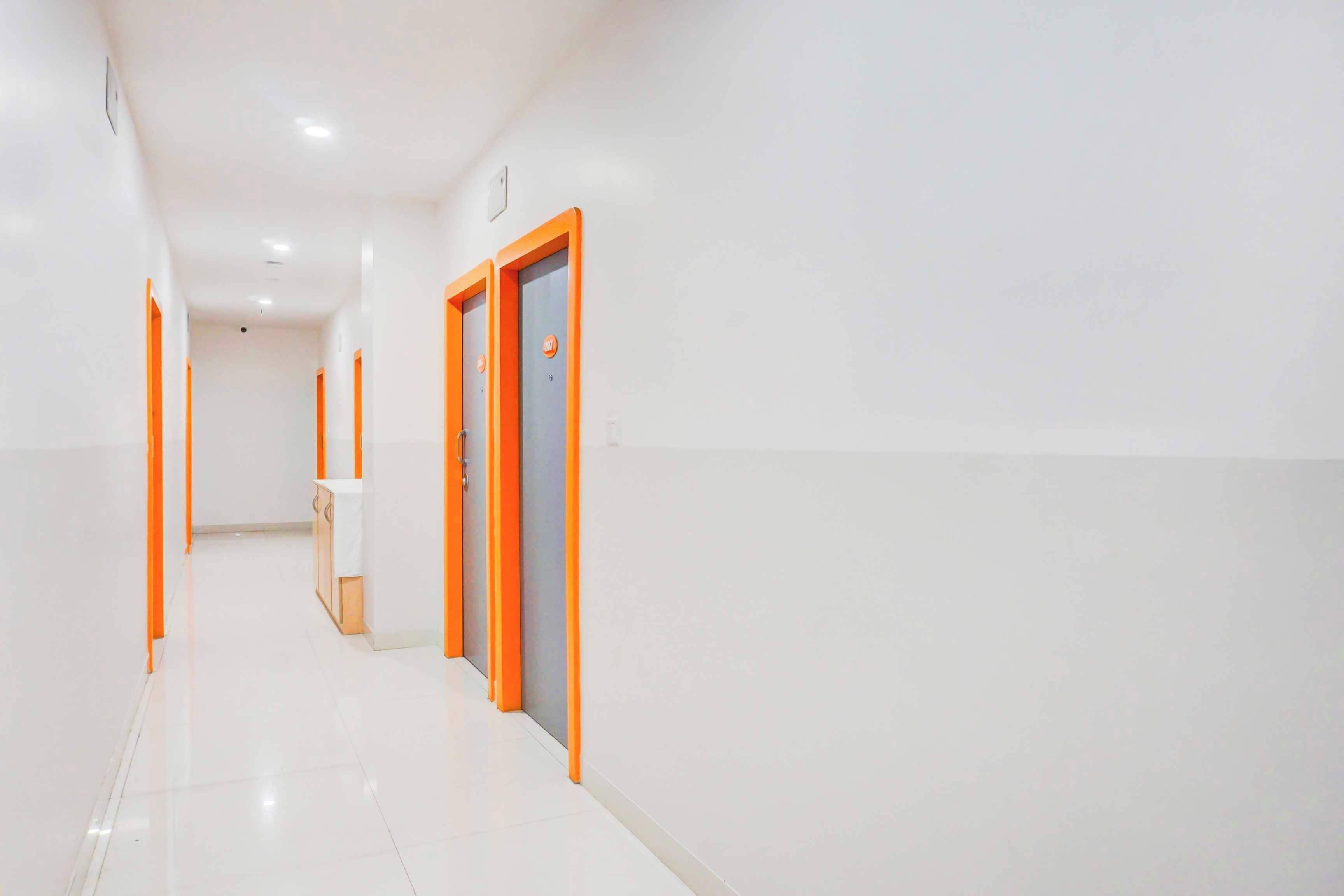 A corridor with white walls and orange doors, leading to a room with a white countertop and cabinets.