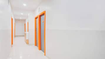 A corridor with white walls and orange doors, leading to a room with a white countertop and cabinets.