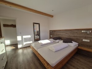 Een slaapkamer met een houten hoofdeinde, een bed met witte lakens, een houten dressoir en een spiegel aan de muur.