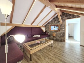 A cozy loft-style living room with a stone wall, wooden beams, a sofa, a coffee table, and a television. - 7_HGG_Michaela by Interhome (Neukirchen am Großvenediger)