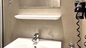 Un baño con un lavabo blanco, un espejo encima y un secador de pelo en la pared.