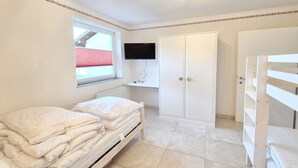 Un dormitorio con cama, armario, televisor y ventana con persianas.