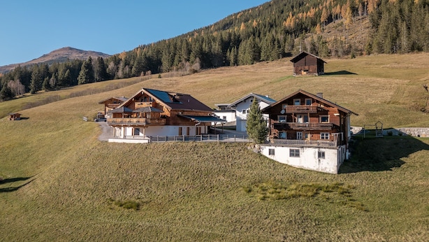 Un albergue de montaña con varias cabañas de madera, un porche cubierto y vistas a una ladera boscosa.