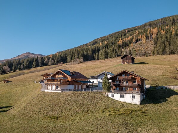 Un chalet de montagne comprenant plusieurs cabanes en bois, un patio couvert et une vue sur une colline boisée.