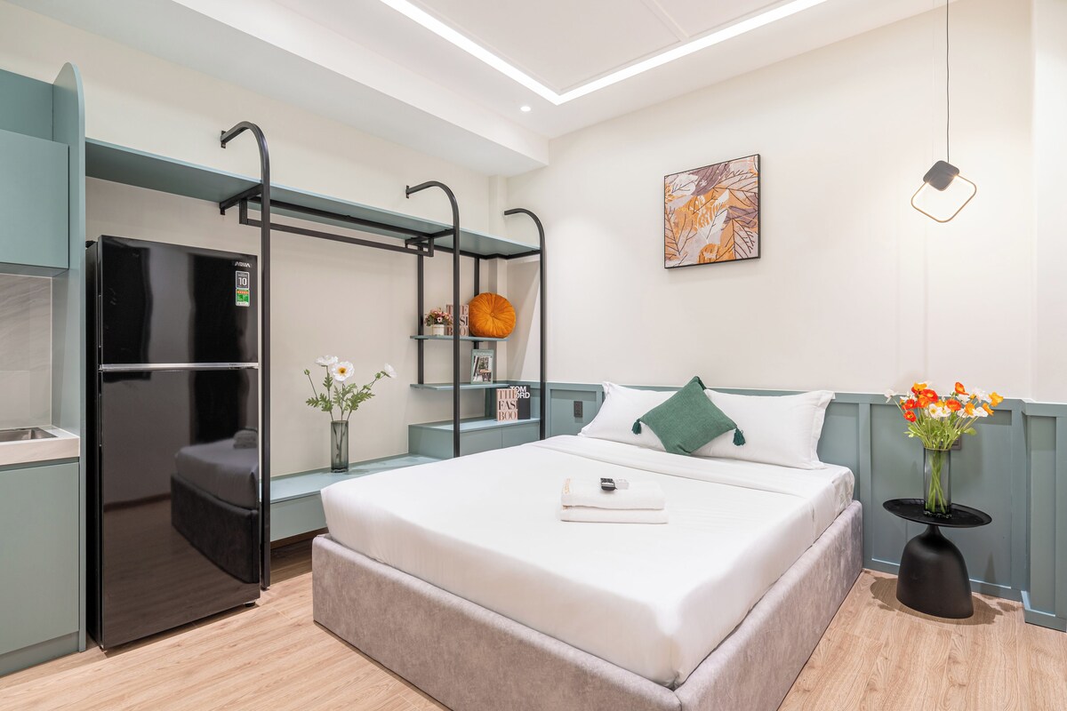 Een moderne hotelkamer met een bed, een inbouwkast, een kitchenette en een nachtkastje met een bloevas.