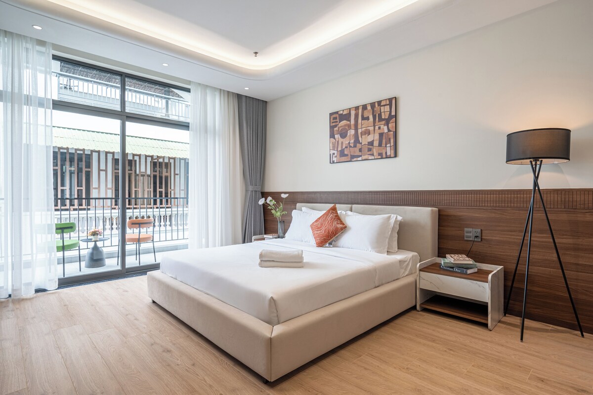 Een moderne hotelkamer met een groot bed, een nachtkastje met een lamp en uitzicht op het omliggende gebied.