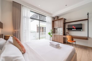 Een hotelkamer met een bed, een bureau, een stoel, een televisie en een balkon met uitzicht.