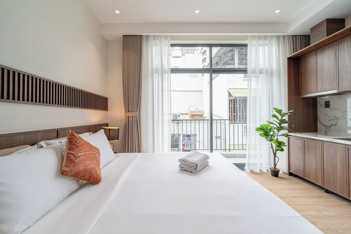 Een moderne hotelkamer met een groot bed, uitzicht op de stad vanaf een balkon en een kitchenette.