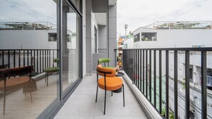 Varanda com divisória de vidro, mesa de madeira, duas cadeiras e vista para a paisagem urbana.
