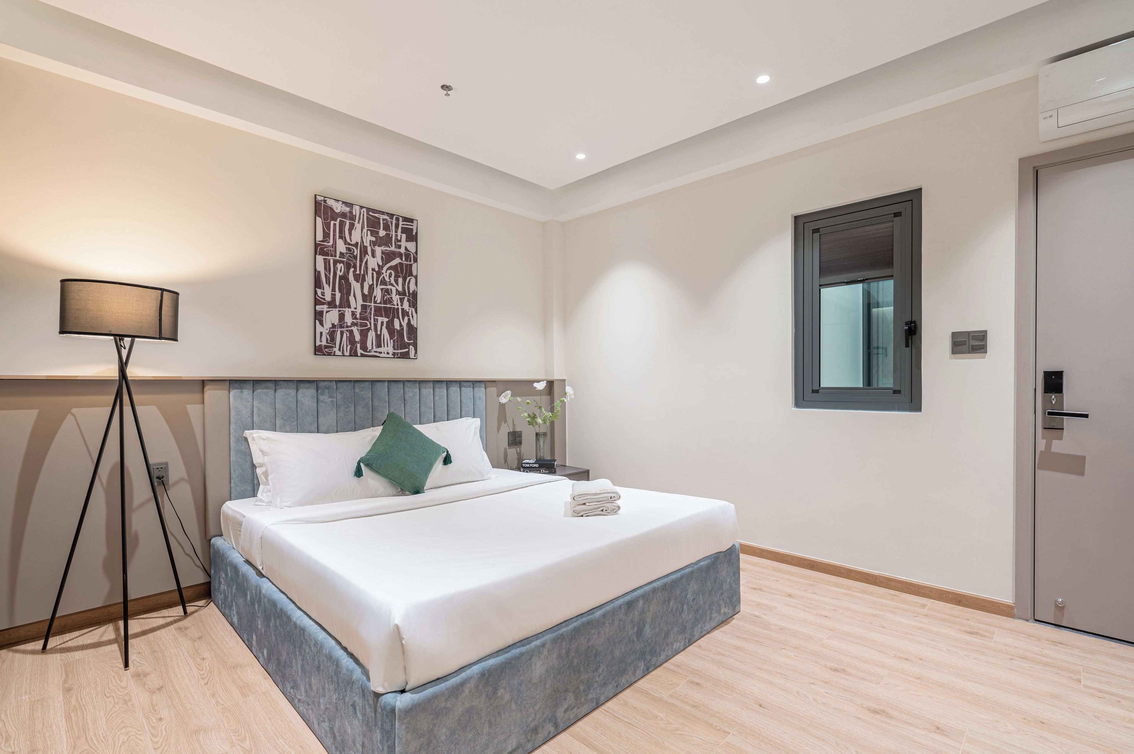 A hotel room with a bed, bedside table, lamp, artwork, and a door.
