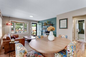 A dining area with a round wooden table, floral-patterned chairs, a vase with flowers, and a bookshelf with decorative items. - Hot Tub Hideaway - Firepit - Big Families (Loveland)