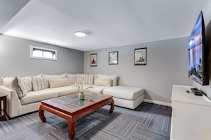 A modern living room with a sectional sofa, a coffee table, and a flat-screen TV mounted on the wall. - Hot Tub Hideaway - Firepit - Big Families (Loveland)