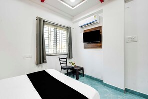 Habitación de hotel con cama, ventana con cortinas, una silla, una mesita con flores y un equipo de aire acondicionado.