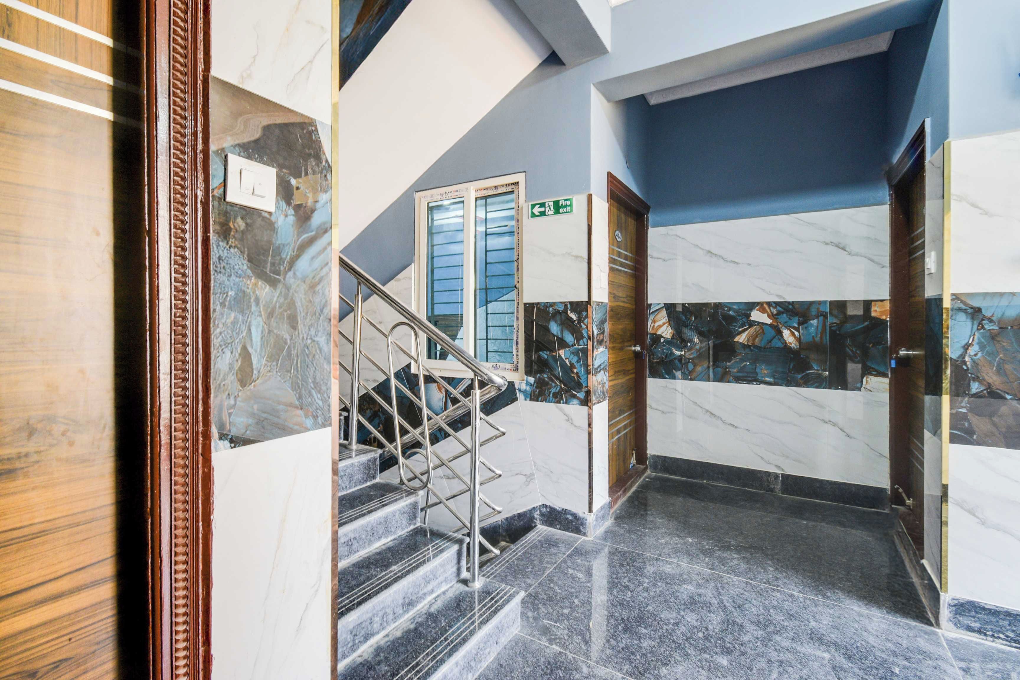 A marble-floored hallway with a staircase, a fire exit sign, and a door with a wooden frame.