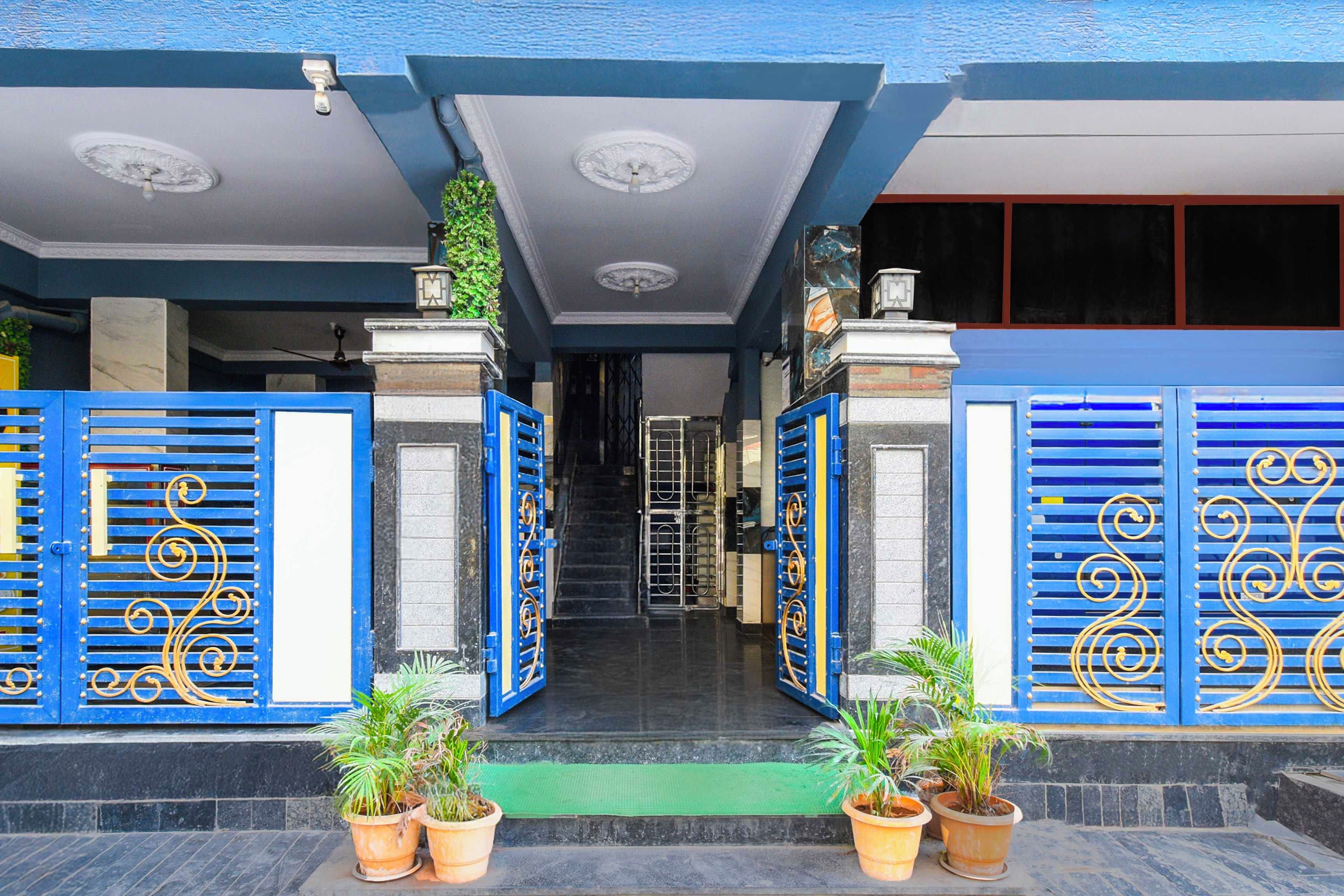 A building entrance with blue decorative gates, a green mat, and potted plants.
