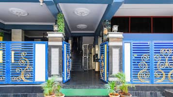 A building entrance with blue decorative gates, a green mat, and potted plants.