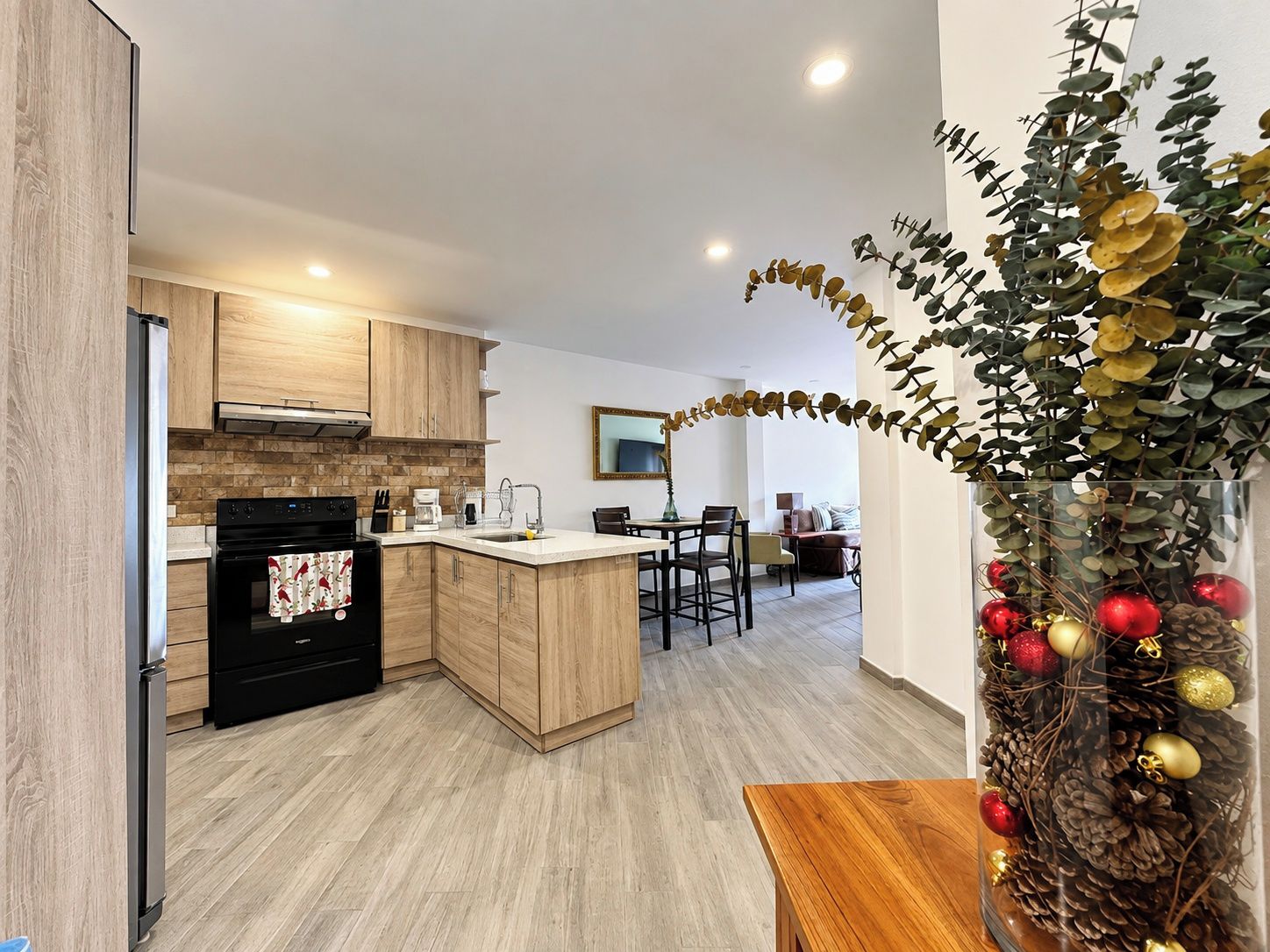 A modern kitchen with wooden cabinets, a black oven, and a dining area with a table and chairs.