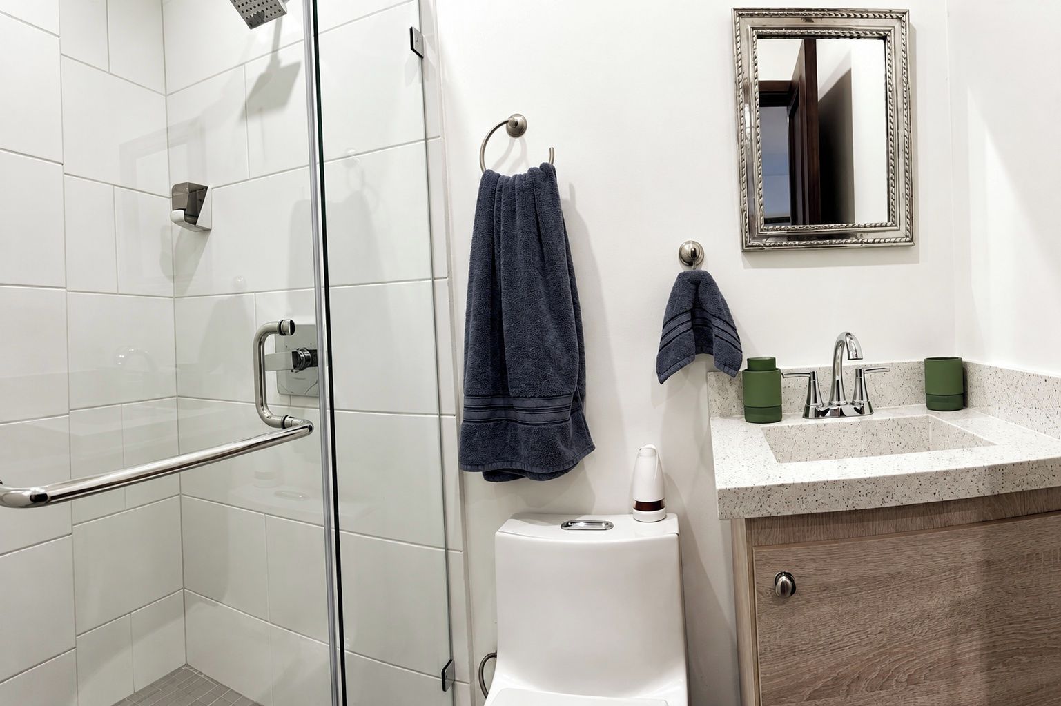 A modern bathroom with a glass shower enclosure, a toilet, a sink with a mirror, and two towels hanging on hooks.