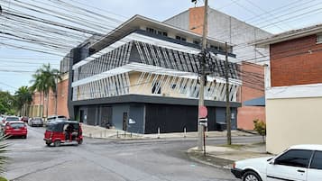 A modern building with a unique geometric facade, a street with cars and a tuk-tuk, and a clear sky.