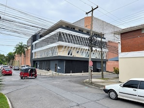 A modern building with a unique geometric facade, a street with cars and a tuk-tuk, and a clear sky.