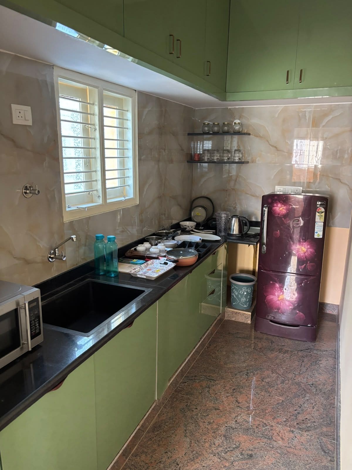 Una cocina con un fregadero, un microondas, un refrigerador y una ventana con persianas.