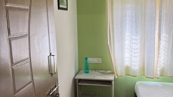 Una habitación con una puerta identificada con el número '102', una cama, una mesita con una botella de agua y una ventana con cortina.