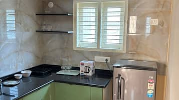 Una cocina con gabinetes verdes, un refrigerador de acero inoxidable, una encimera negra y una ventana con persianas.