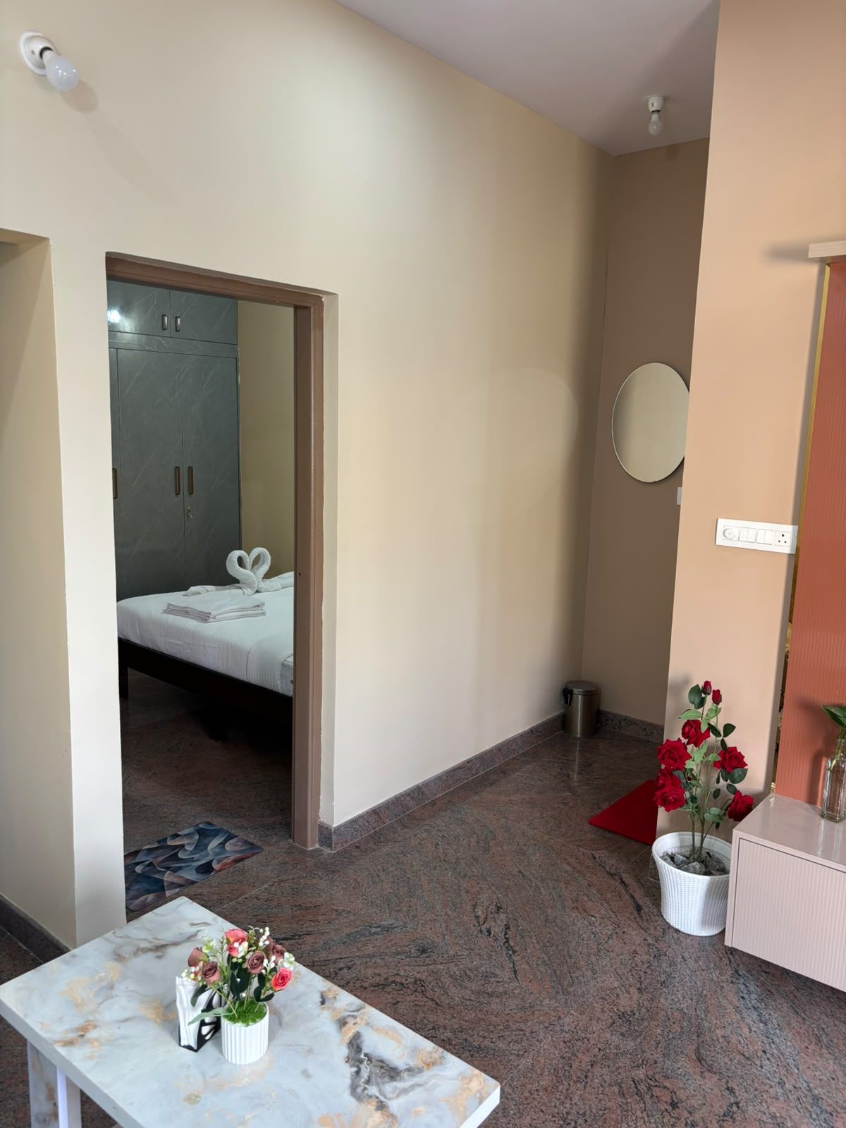 Una habitación de hotel con una cama, una mesa con un florero, un espejo y un armario.