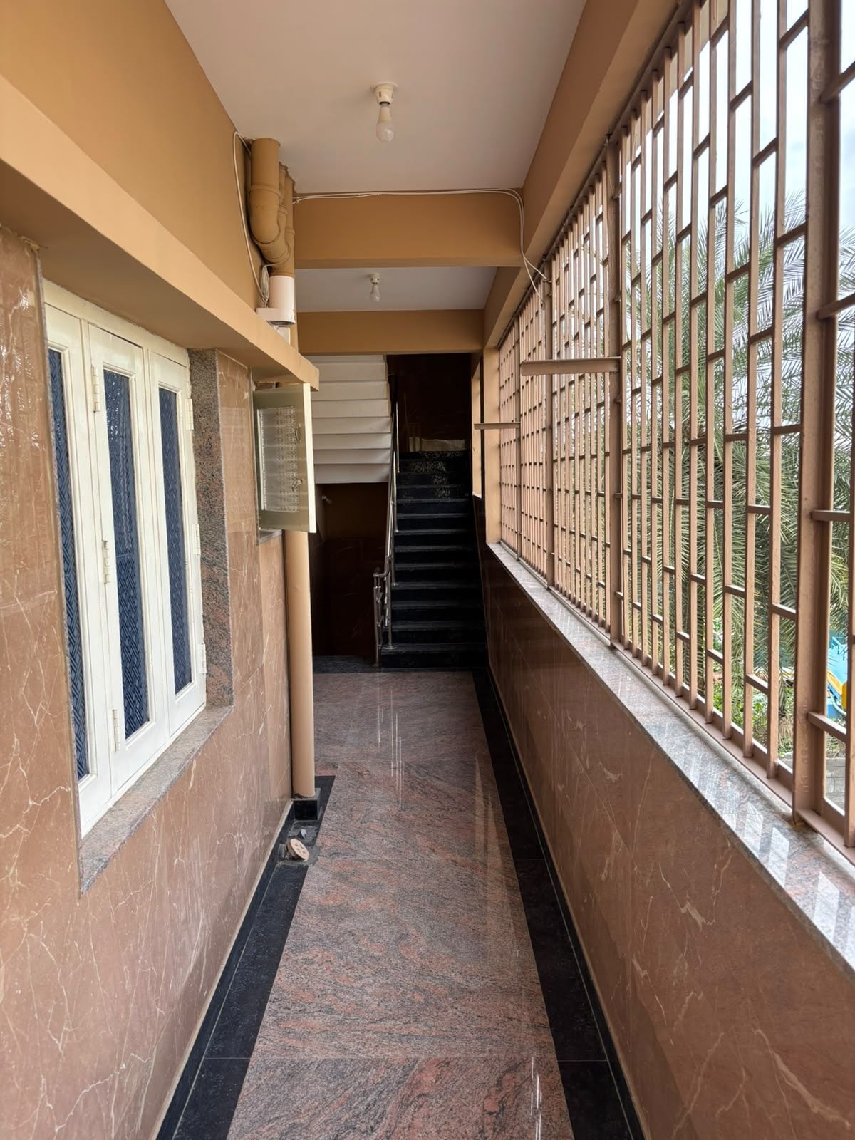 A corridor with a marble floor, a staircase, and a window with metal bars.