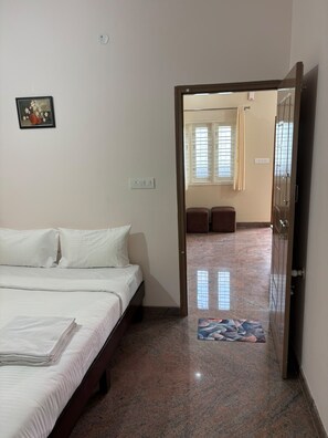 A hotel room with a bed, a small table, a picture on the wall, and a door leading to another room. - Olive Service Apartment  (Anekal)