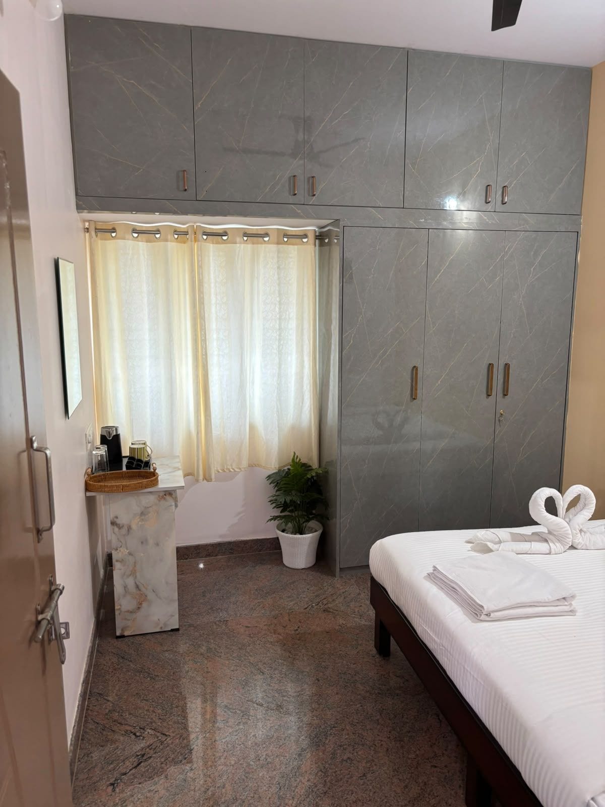 Ein Schlafzimmer mit Bett, Kleiderschrank, Badezimmer mit Duschvorhang, einem Blumentopf und einem kleinen Tisch mit Toilettenartikeln.