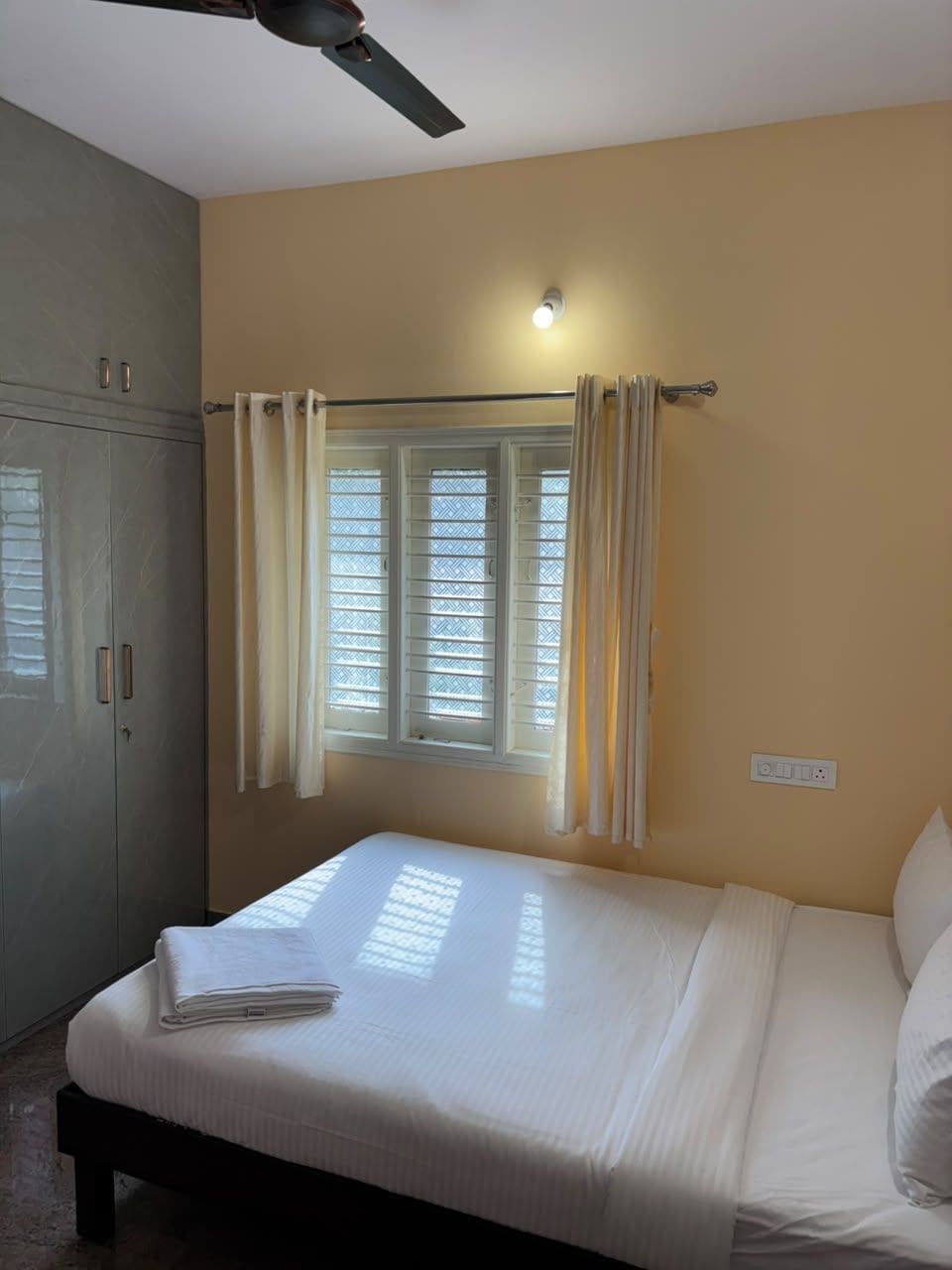 Un dormitorio con cama, ventana con cortinas, ventilador de techo y armario.
