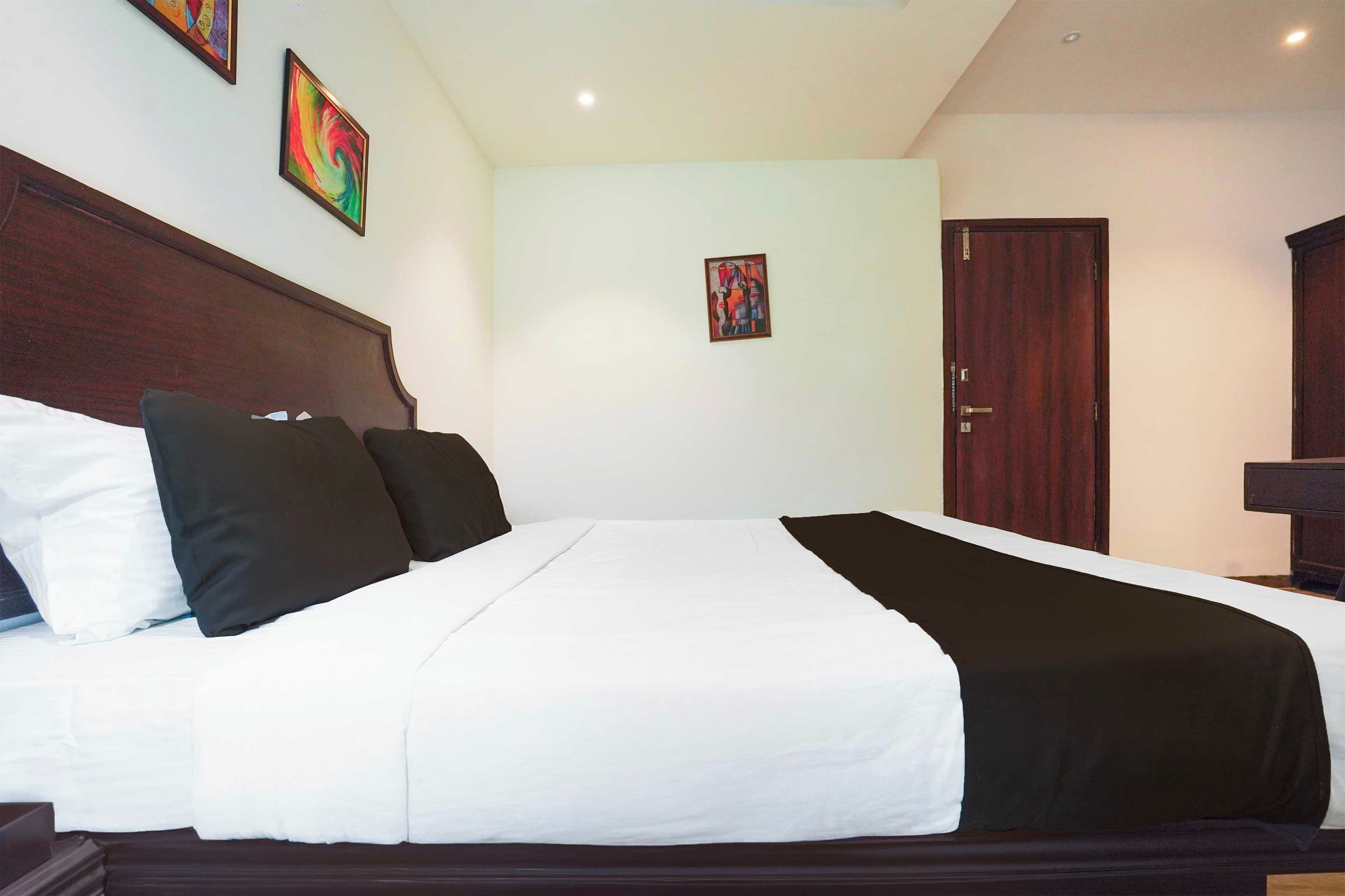 Una habitación de hotel con una cama grande, un cabecero de madera, dos cuadros colgados en la pared y una puerta.