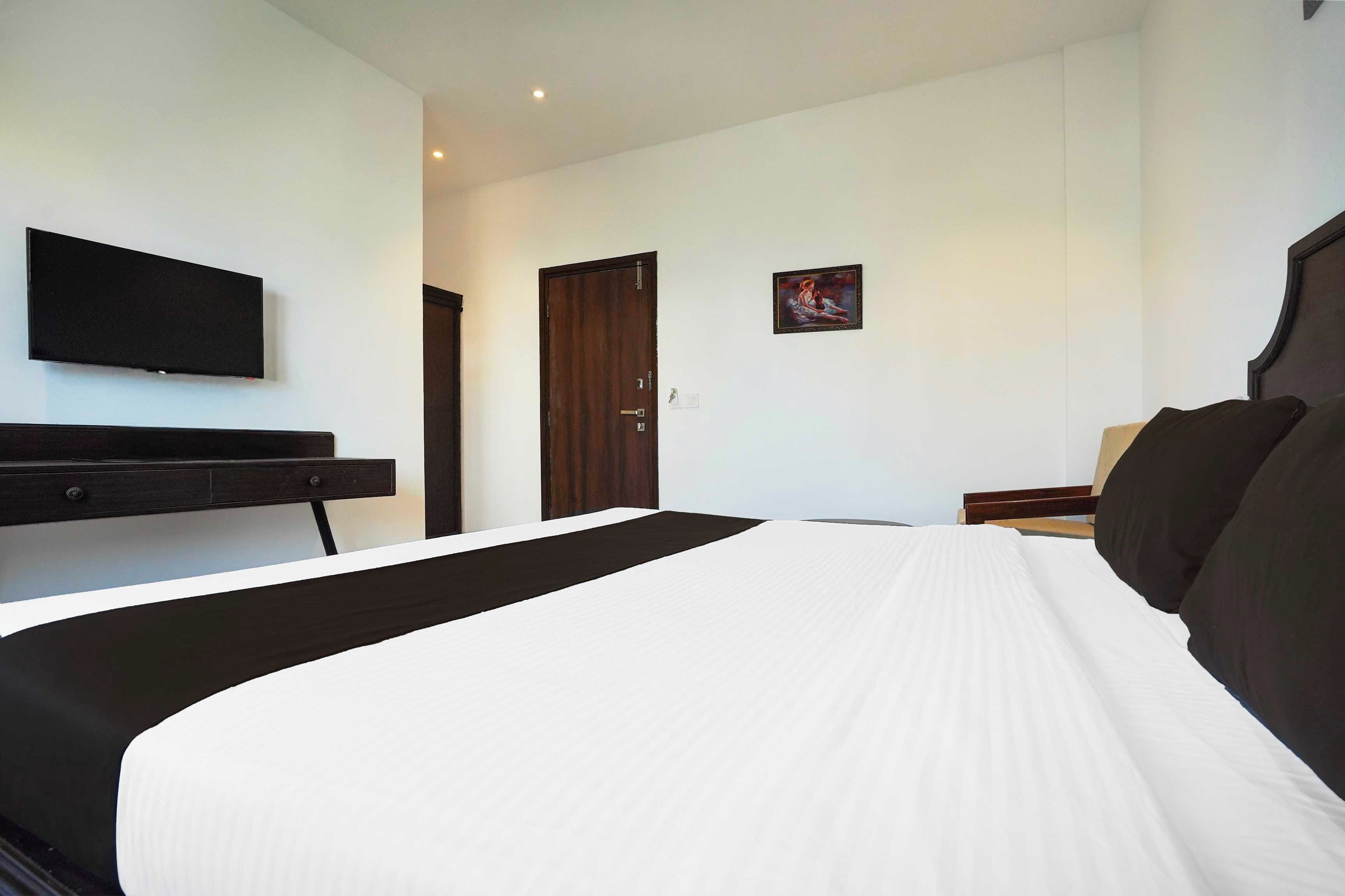 Habitación de hotel con cama, un televisor de pantalla plana en la pared, una puerta y un pequeño cuadro.