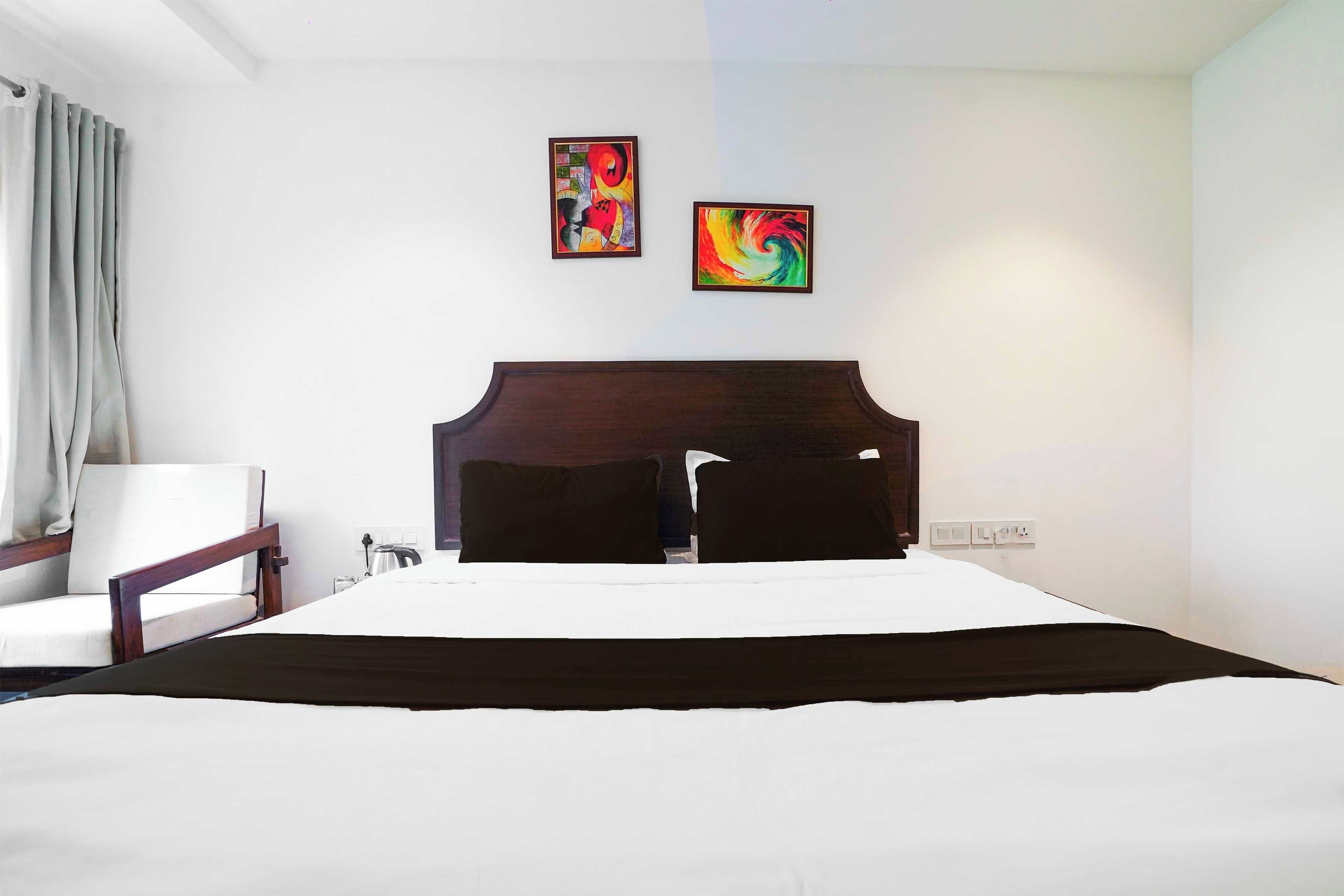 Una habitación de hotel con una cama grande, un cabecero de madera, una silla y dos cuadros en la pared.
